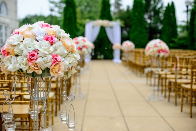 An outdoor wedding ceremony with pink and peach flowers on golden chairs